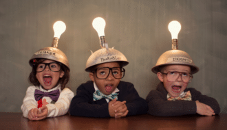 3 children being googy wearing helmets with lightbulbs on them to highlight the question, "What is Classroom Management?"