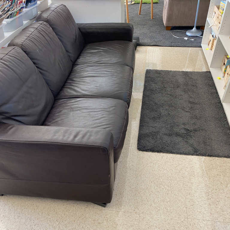 Black loveseat, grey carpet, white bookshelf for how to decorate a classroom in a cozy way.