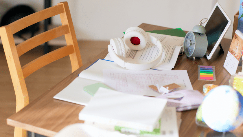 messy student desk strewn with papers, headphone and a computer showing poor executive skills.